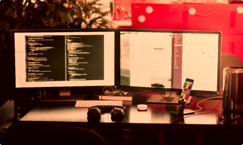 Two monitors on a desk displaying code and other images relating to the website maintenance services of a marketing agency