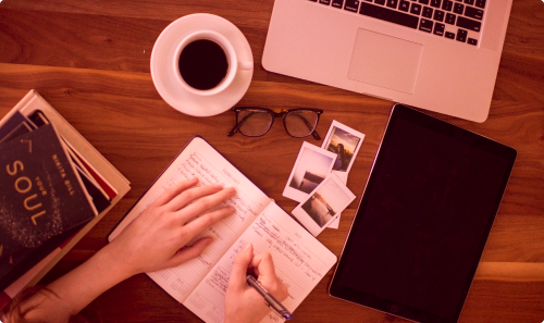 Person writing in a notebook surrounded by books and a laptop as part of content creation marketing services